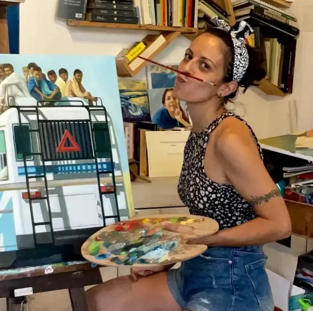 Sara Longhi nel suo studio, con tavolozza e pennello, davanti a un dipinto in lavorazione